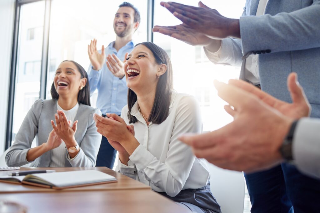Group of business professionals smiling and applauding during a meeting.