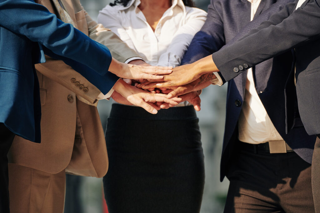 A group of corporate professionals demonstrating teamwork by joining hands.