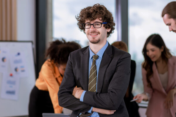 A young sales professional standing confidently with his team in the background.