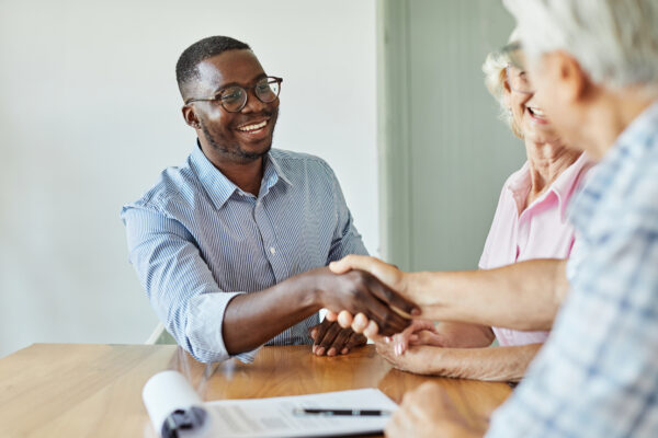 A young sales representative shaking hands with his client after having a positive meeting with them.