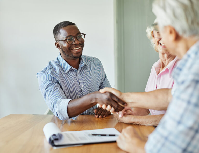 A young sales representative shaking hands with his client after having a positive meeting with them.