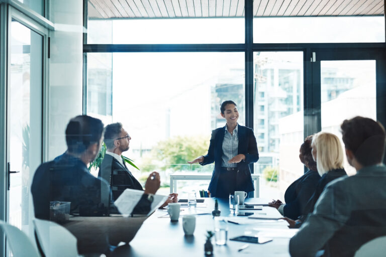 A young professional discussing in front of her colleagues in a bright office setting.