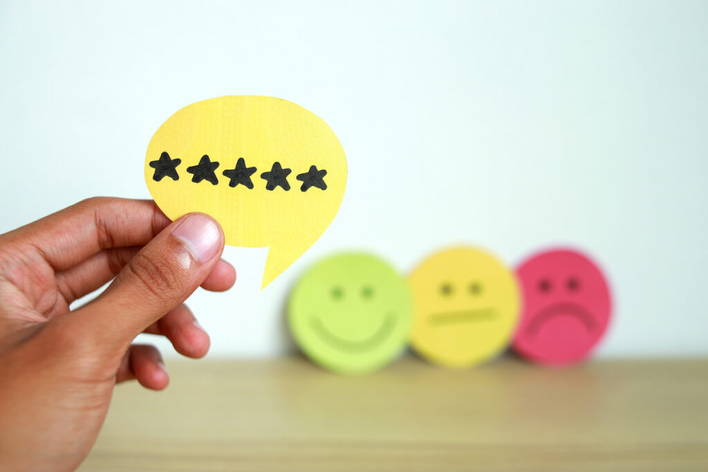 A hand is holding a yellow paper cut out of a speech bubble, with five black stars printed on it.